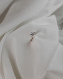 Μονόπετρο δαχτυλίδι γάμου με κεντρικό διαμάντι και πέτρες brilliant περιμετρικά κατασκευασμένο από λευκόχρυσο, επάνω σε λευκό μετάξι.