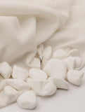 Μονόπετρο δαχτυλίδι με διαμάντι κατασκευασμένο από λευκόχρυσο, με πλαϊνές πέτρες από μικρότερα διαμάντια, τοποθετημένο επάνω σε λευκό ύφασμα με βότσαλα.