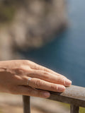 Λευκόχρυσο μονόπετρο δαχτυλίδι με διαμάντι και καστόνι που αγκαλιάζει την πέτρα σε σχήμα φλόγας, φορεμένο σε γυναικείο χέρι.