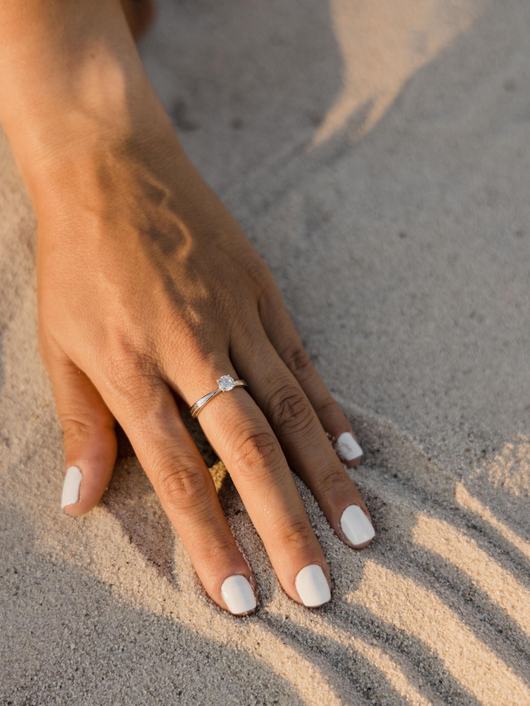 Μονόπετρο δαχτυλίδι με διαμάντι κατασκευασμένο από λευκόχρυσο και καστόνι σε σχήμα "V", φορεμένο σε γυναικείο χέρι.