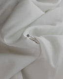 Μονόπετρο δαχτυλίδι γάμου με κεντρικό διαμάντι και πέτρες brilliant περιμετρικά κατασκευασμένο από λευκόχρυσο, ακουμπισμένο επάνω σε λευκό μετάξι.