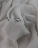 Μονόπετρο δαχτυλίδι φλόγα με διαγώνια πλέξη και πλαϊνές πέτρες, κατασκευασμένο από λευκόχρυσο 14 καρατίων και ζιργκόν σε λευκό σεντόνι