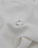 Λευκόχρυσο μονόπετρο με διαμάντι και καστόνι σχήματος V σε λευκό ύφασμα.