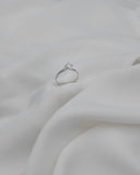 Λευκόχρυσο μονόπετρο δαχτυλίδι με διαμάντι και δέσιμο φλόγας επάνω σε λευκό ύφασμα.
