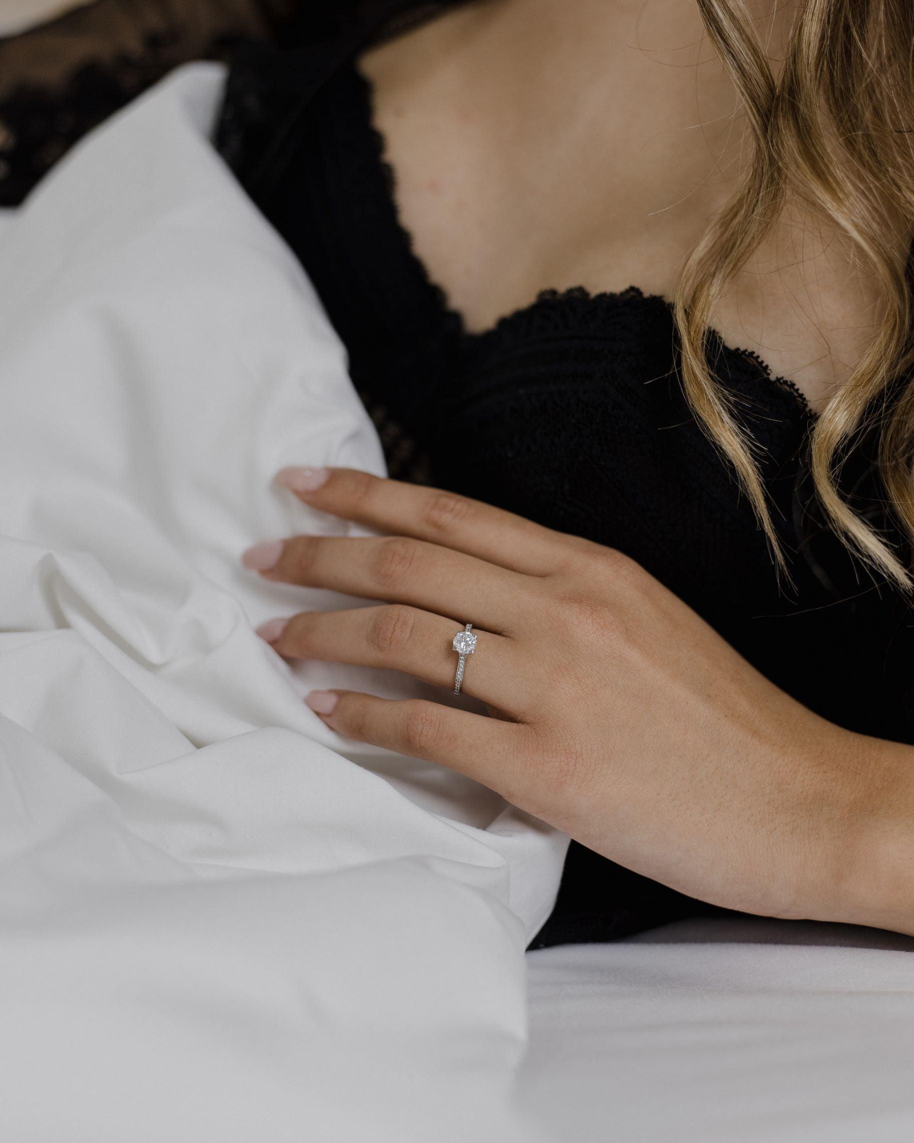 Λευκόχρυσο μονόπετρο με διαμάντι και πλαϊνές πέτρες από μικρότερα διαμάντια φορεμένο σε γυναικείο χέρι.