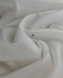Λευκόχρυσο μονόπετρο με διαμάντι και πλαϊνές πέτρες επάνω σε λευκό σεντόνι.