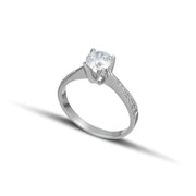 Λευκόχρυσο μονόπετρο με διαμάντι και πλαϊνές πέτρες από μικρότερα διαμάντια φορεμένο σε γυναικείο χέρι.