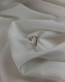 Μονόπετρο δαχτυλίδι γάμου με διαμάντι κατασκευασμένο από λευκόχρυσο, με διαγώνια πλέξη και καστόνι με έξι δόντια, ακουμπισμένο επάνω σε λευκό μετάξι