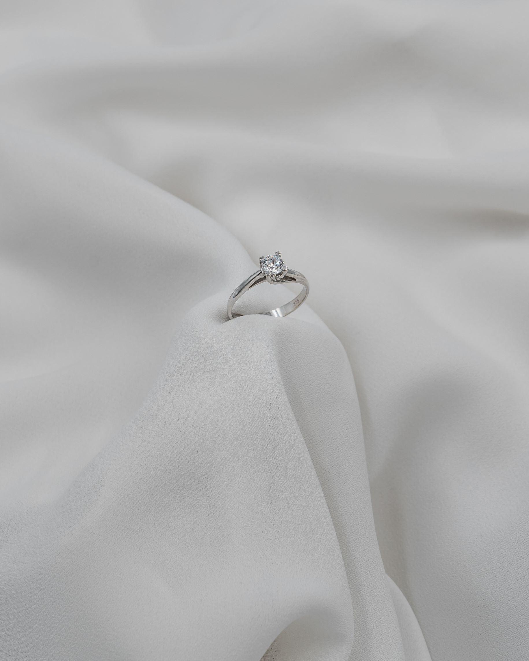 Λευκόχρυσο μονόπετρο δαχτυλίδι φλόγα με διαμάντι σε λευκό ύφασμα. 