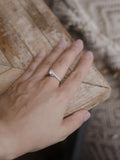 Μονόπετρο δαχτυλίδι με κεντρικό διαμάντι round cut και πλαϊνές πέτρες από μικρότερα διαμάντια, κατασκευασμένο από λευκόχρυσο φορεμένο σε γυναικείο χέρι.