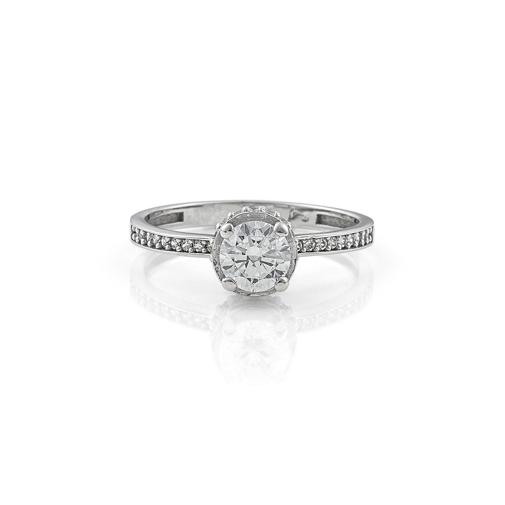 Μονόπετρο δαχτυλίδι με κεντρικό διαμάντι round cut, πλαίνές πέτρες από μικρότερα διαμάντια και στρογγυλό καστόνι σε σχήμα κορώνας κατασκευασμένο από λευκόχρυσο.