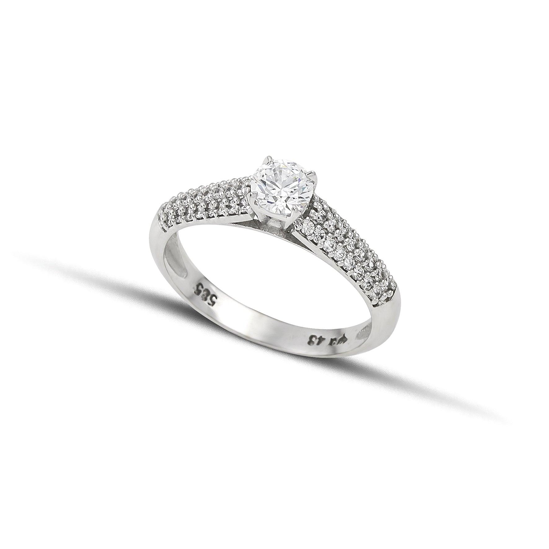 Μονόπετρο δαχτυλίδι με κεντρικό διαμάντι round cut και πλαϊνές πέτρες από μικρότερα διαμάντια, κατασκευασμένο από λευκόχρυσο.