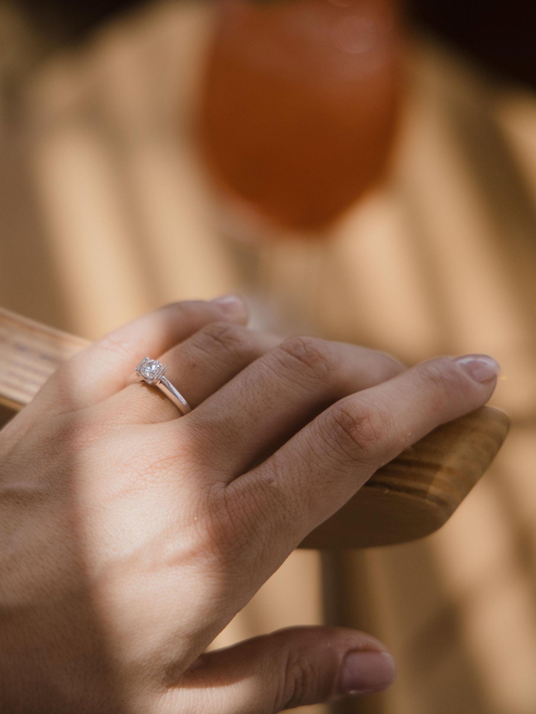 Mονόπετρο δαχτυλίδι με διαμάντι κατασκευασμένο από λευκόχρυσο με καστόνι σχήματος "V", φορεμένο σε γυναικείο χέρι.