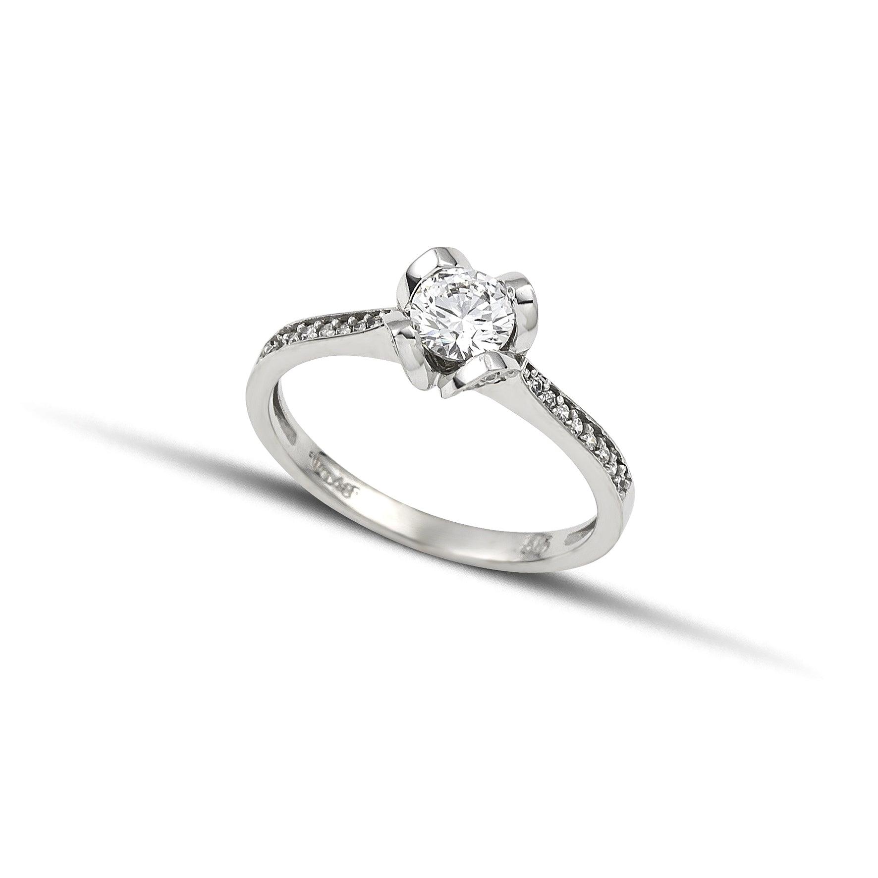 Μονόπετρο δαχτυλίδι με διαμάντι και πλαϊνές πέτρες από μικρότερα διαμάντια, κατασκευασμένο από λευκόχρυσο με καστόνι σε σχήμα λουλουδιού.