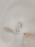Mονόπετρο δαχτυλίδι με διαμάντι κατασκευασμένο από λευκόχρυσο με καστόνι σχήματος "V" και πλαϊνές πέτρες από μικρότερα διαμάντια, επάνω σε λευκό ύφασμα.