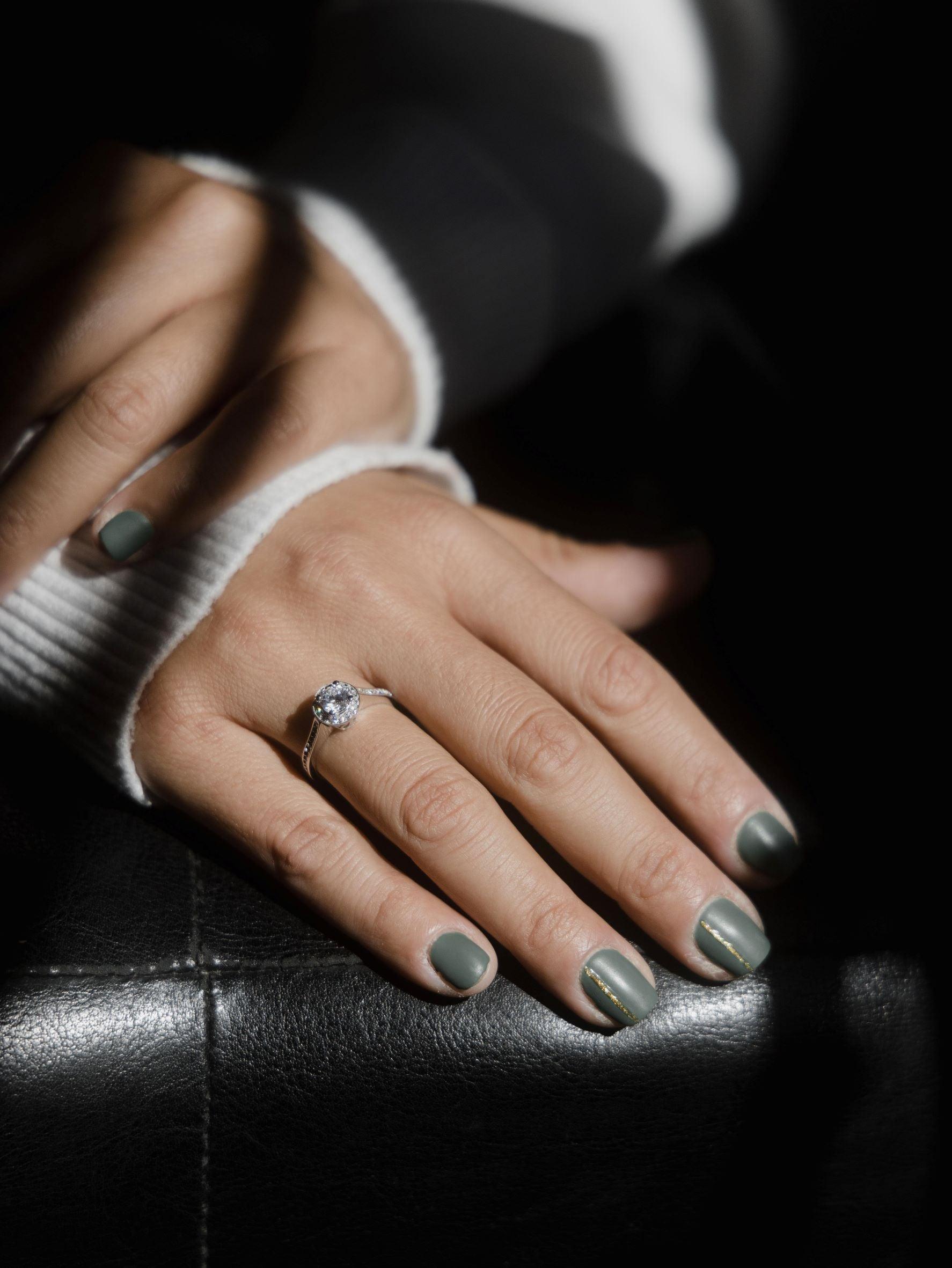 Μονόπετρο δαχτυλίδι ροζέτα με κεντρικό διαμάντι round cut, πλαίνές πέτρες από μικρότερα διαμάντια και στρογγυλό καστόνι, κατασκευασμένο από λευκόχρυσο φορεμένο σε γυναικείο χέρι.